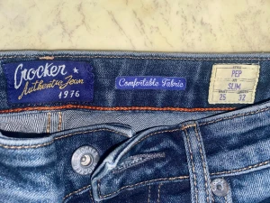 Crocker Slim Fit Jeans Pep 25/32 - Snygga blå jeans från Crocker i modellen Pep med slim fit. Klassisk femficksdesign, orange kontrastsömmar och bekvämt denimtyg. Passar dig som gillar smalare siluett och autentisk jeansstil. Midjan är normal och materialet är slitstarkt bomullsjeans. Jeansen är klippta nertill och därför passar 28-30 längd 
