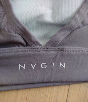 Grå sportig linnetopp från NVGTN - Säljer en grå linnetopp från NVGTN i storlek L, perfekt för träning. Toppen har breda axelband, rundad halsringning och är tillverkad i mjukt, stretchigt syntetmaterial med 75% nylon och 25% spandex. Snygg och enkel design med logga framtill.