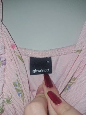 Ljusrosa blommig klänning Gina Tricot - Supersöt ljusrosa kortklänning från Gina Tricot med blommigt mönster i lila, blått, rosa och orange. Klänningen har breda axelband, lätt rynk vid bysten och en flowy passform. Perfekt för sommarens alla tillfällen!