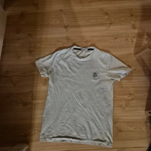 Vit Moncler t-shirt med broderad logga - Vit t-shirt från Moncler med klassisk rund hals och broderad logga på bröstet. T-shirten är i bomull och har en enkel, stilren design som passar perfekt till jeans eller shorts. Skön passform och diskret branding för en clean look. kom med bud och frågor 