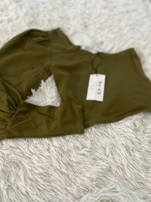 Khakigrön oneshoulder croppad topp NA-KD - Säljer en khakigrön croppad topp från NA-KD i storlek XS. Modellen har en puffärm på ena sidan och är oneshoulder, vilket ger en cool och trendig look. Materialet är mjukt och stretchigt, perfekt för att sticka ut med en unik siluett.
