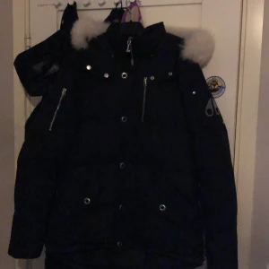 Svart Moose Knuckles dunjacka med päls - Säljer en svart dunjacka från Moose Knuckles med vit päls på huvan perfekt för kalla vinterdagar och har en riktigt schysst streetstil. Pris kan diskuteras också
