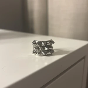 Silvrig ring med nitar - Cool och chunky ring i silverfärgad metall med tre rader av spetsiga nitar framtill. Ringen har en bred design som verkligen sticker ut och ger en edgy vibe till din stil. Perfekt för dig som gillar statement-smycken och vill ha något unikt. Väldigt bra skick! Helt ny❤️
