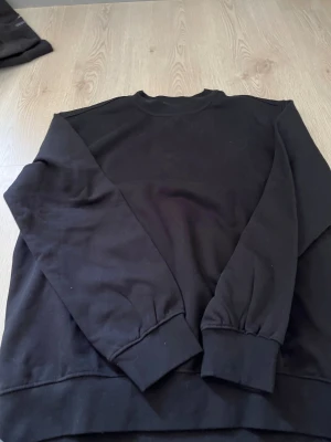 Svart sweatshirt från Fristads M - Svart sweatshirt från Fristads i storlek M. Tröjan har rund hals, långa ärmar och breda muddar vid ärmslut och nederkant. Tillverkad i mjuk bomullsmix som är skön att ha på sig. Enkel och stilren design som funkar till många olika outfits.