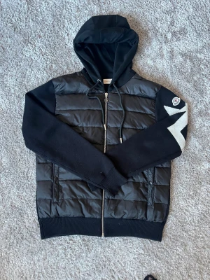 Moncler cardigan  - Tjena, säljer en Moncler cardigan i storlek M, detta är modellen med ett M på höger axel och otroligt snygg, cardiganen är perfekt för dig som vill ha något till vintern men inte för tjockt och puffigt.