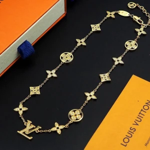 Louis Vuitton Monogram halsband - Exklusivt halsband från Louis Vuitton med ikoniska monogramblommor och LV-logga. Finns i både guld- och silverfärg, dekorerat med glittrande detaljer. Kedjan är tunn och smycket har flera små hängande emblem som ger en lyxig vibe. Perfekt för dig som gillar designeraccessoarer.