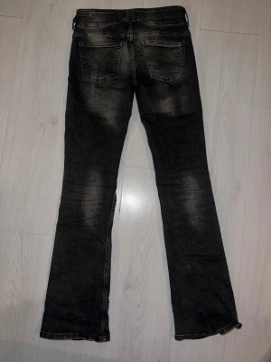 Bootcut svarta jeans från Bershka - Säljer ett par svarta jeans från Bershka med snyggt slitna detaljer och bootcut passform. Jeansen har klassiska fem fickor, hällor för bälte och dragkedja med knapp. Materialet är stretchigt denim som sitter skönt och formar sig efter kroppen.