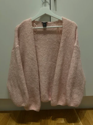 Ljusrosa stickad kofta från Lindex - Mysig och oversized ljusrosa stickad kofta från Lindex. Koftan har långärmade ballongärmar och är öppen framtill utan knappar. Perfekt för lager-på-lager och chill dagar. Supermjuk känsla och fluffigt material. 