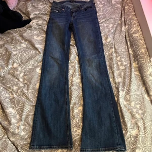 Blå bootcut jeans från Lindex, stl 34 - (Har ett hål vid vänster bakficka se bild 3)                                                                               Snygga blå jeans från Lindex i storlek 34 med klassisk bootcut passform. Jeansen har fem fickor, slitna detaljer vid ena fickan och är gjorda i mjukt denimtyg. Perfekt för dig som gillar retrovibbar och vill ha ett par jeans med lite extra karaktär.