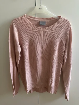Ljusrosa stickad tröja med rund hals - Mysig ljusrosa stickad tröja från Vero Moda med rund hals och ribbade detaljer. Tröjan har långärmade ärmar och en enkel, clean look som är lätt att matcha med jeans eller kjol