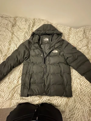 Svart pufferjacka från The North Face XL - Svart pufferjacka från The North Face i storlek XL. Jackan har huva, dragkedja och två stora fickor framtill. Klassisk quiltad design med logga på bröstet och ryggen. Perfekt för kalla dagar och riktigt snygg streetstil. Jag är mellan M/L de passar perfekt