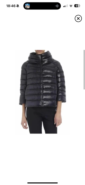 Svart dunjacka från Herno Iconico - Snygg svart dunjacka från Herno Iconico med glansig finish och bred krage. Jackan har trekvartsärm, quiltad design och stängs med knappar framtill. Storlek 46 (italiensa storlekar). Inga effekter