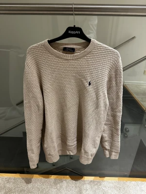 Beige stickad tröja Polo Ralph Lauren - Snygg beige stickad tröja från Polo Ralph Lauren storlek L fast kan också passa som en storlek M med grovt vävt mönster och klassisk rund hals. Tröjan har långärmade ribbade muddar och den ikoniska broderade loggan på bröstet. Perfekt för dig som gillar stilrena och tidlösa plagg. Skriv efter minsta lilla fundering!! Pris kan diskuteras!!