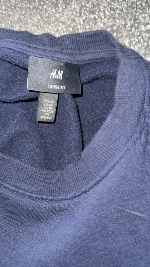Mörkblå loose fit tröja från H&M - Säljer en mörkblå crewneck från H&M i loose fit-modell. Tröjan har rund hals, långa ärmar och ribbade muddar vid ärmslut och nederkant. Perfekt för chill dagar och enkel att matcha med jeans eller joggers. Passar dig också som har S
