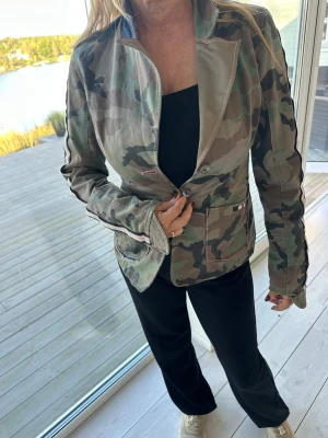 Camouflage kavajjacka Triple Five - Snygg kavajjacka från Triple Five med grön och brun camouflageprint och coola ränder längs ärmarna. Jackan har två framfickor, knappar framtill och bälte bak. Mycket svår att få tag i!😍