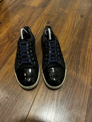 Svarta sneakers från Lanvin - Snygga svarta sneakers från Lanvin med blank tå och sidor i mocka. Skorna har rund tå, snörning och vit platt sula. Perfekt för dig som gillar stilrena och exklusiva sneakers med cool kontrast mellan material. Skorna passar till allt kontakta mig vid minsta fundering pris går att diskutera ☺️