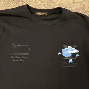 Svart tröja från Louis Vuitton med molnmönster - Snygg svart tröja från Louis Vuitton med ett unikt molnmönster i blått och vitt. Tröjan har en klassisk passform och rund halsringning. Perfekt för dig som vill ha något stilrent men ändå iögonfallande.