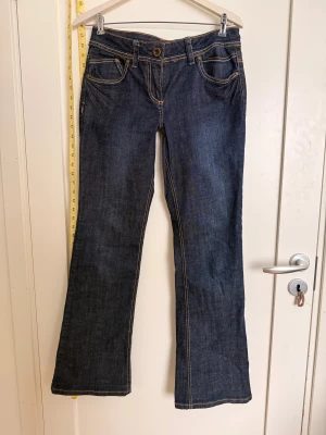 Blå bootcut jeans Dorothy Perkins - Snygga mörkblå bootcut jeans från Dorothy Perkins med kontrastfärgade sömmar och coola bakfickor med broderad detalj och knapp. Klassisk femficksmodell och låg midja, tillverkade i jeansmaterial. Perfekt för dig som gillar retrovibbar och bekväm passform.  Omsydda till lågmidjade så kan vara lite tajta runt låren