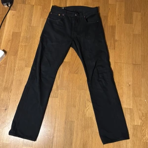 (NYA!)Svarta Levi's 501 jeans W30 L32 - Säljer ett par svarta Levi's 501 jeans i klassisk rak modell. Byxorna har fem fickor, knappgylf och detaljer i kopparfärg. Tillverkade i slitstarkt jeanstyg och passar perfekt till en clean och tidlös stil.