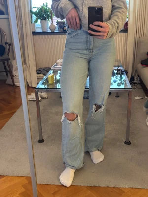 Ljusa ripped jeans från Zara - Säljer ett par ljusblå jeans från Zara med hög midja och raka, vida ben. Jeansen har snygga slitningar och hål vid knäna. Klassisk femficksmodell och tillverkade i jeansmaterial.