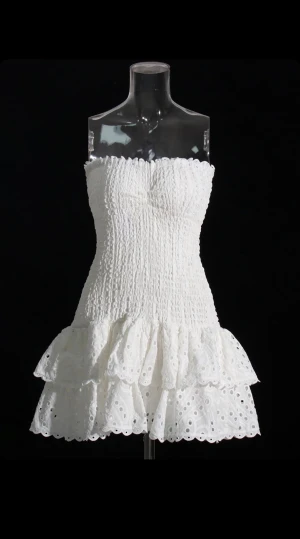 Vit axelbandslös klänning Gina Tricot - Supersöt vit kortklänning från Gina Tricot i storlek S. Axelbandslös modell med smockad överdel och två volanger nedtill. Klänningen har broderade detaljer och är tillverkad i bomull, perfekt för sommarens alla tillfällen. Fräsch och feminin look!