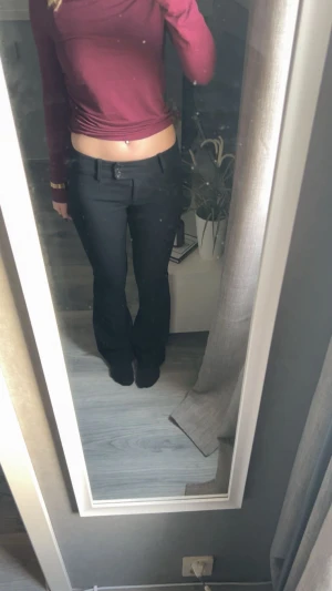 Svarta lågmidjade bootcut kostymbyxor - Snygga svarta kostymbyxor med bootcut-snitt och klassisk midja. Byxorna har bälteshällor, knapp och dragkedja framtill. Passar perfekt till en trendig look och är enkla att matcha med olika toppar. Materialet känns mjukt och har en stilren finish.