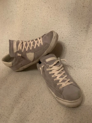 Grå Philippe Model sneakers i mocka pris ej hugget i sten!! - Snygga grå sneakers från Philippe Model i mjuk mocka med beige detaljer och snörning. Skorna har en klassisk låg profil, rund tå och platt sula. Perfekta för dig som gillar stilrena och exklusiva sneakers med en clean look.