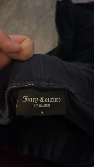 Svarta mjukisbyxor Juicy Couture M - Svarta mjukisbyxor från Juicy Couture i storlek M. Byxorna har en mjuk och glansig sammetstextur, snörning i midjan och bakfickor med guldfärgade knappar. Perfekt för chill dagar och har en klassisk Juicy-look. Marinblåa. En knapp har låsnat vid högra baksidan.