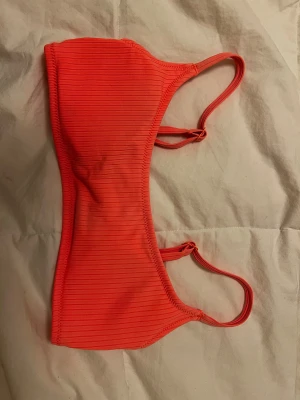 Ribbad orange bikiniöverdel Cubus XS - Snygg bikiniöverdel från Cubus i en stark orange färg med ribbad struktur. Modellen har smala axelband och en cool plastspänne i ryggen. Perfekt för dig som vill sticka ut på stranden i sommar! Materialet är mjukt 💕