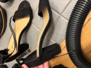 Svarta sandaler med klack från Alley - Snygga svarta sandaler från Alley med bred rem över tårna och justerbart spänne vid ankeln. Skorna har öppen tå och en stabil, fyrkantig klack. Utsidan är i mocka-look och innersulan är ljusbeige för en fräsch kontrast. Perfekta för dig som gillar stilren design.