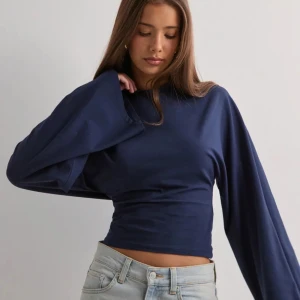 Mörkblå croppad långärmad tröja - Snygg mörkblå croppad tröja med långa, vida ärmar och rund hals. Tröjan har en slim passform som framhäver midjan och är tillverkad i mjukt bomullsmaterial. Perfekt för dig som gillar stilrena och trendiga plagg med lite edge.