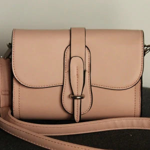 Rosa väska - Snygg rosa axelväska med justerbar axelrem och dekorativ spänndetalj framtill. Väskan har dragkedja bak samt blommigt foder och dragkedja inuti. Enkel och praktisk väska.