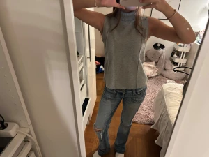 Grå ärmlös polotopp i stickat material - Säljer en stilren grå polotopp i stickat material. Toppen är ärmlös med hög krage och har en rak, något loose passform. Perfekt att matcha med jeans eller kjol för en clean look.