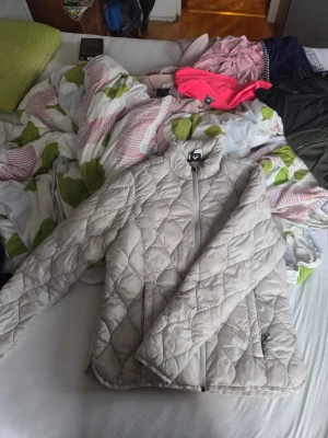 Beige quiltad jacka från McKinley - Säljer en beige quiltad jacka från McKinley i storlek 42. Jackan har lång ärm, hög krage och dragkedja framtill. Den är lätt vadderad och har ett snyggt rutmönster i quiltad stil. Perfekt för kyliga dagar när du vill ha en stilren look.