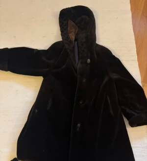 Svart pälsjacka med huva - Mysig svart pälsjacka med huva och knäppning framtill. Jackan har en lyxig känsla med mjukt foder och breda ärmar. Perfekt för kalla dagar när du vill hålla stilen och värmen. Snygg och tidlös design som passar till många outfits.