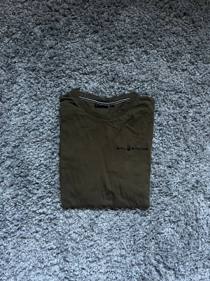 Olivgrön t-shirt från Sail Racing - Olivgrön t-shirt från Sail Racing med diskret logga på bröstet. Klassisk rund hals och korta ärmar. Tillverkad i mjuk bomull som känns skön mot huden. Perfekt för dig som gillar stilrena och enkla plagg med sportig touch.