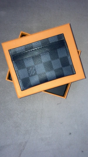  rutig kortfodral i skinn - Snyggt kortfodral från mörkblått och svart skinn med klassiskt rutigt mönster. Perfekt för kort och sedlar, stilren design med flera fack. Kommer i original orange ask.