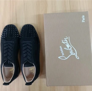 Christian Louboutin svarta sneakers med nitar - Svarta sneakers från Christian Louboutin med rund tå och platt sula. Ovandelen är i mocka och har snörning samt är täckt med svarta nitar framtill för en edgy look. Insidan är ljusbeige och sulan har den klassiska röda undersidan.