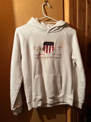 Vit hoodie från GANT med broderad logga - Vit hoodie från GANT med broderad logga och emblem på bröstet. Är från kidsbrandstore så är storlek 158/164 (13-14år). Skulle säga att det är som typ S för de är de jag har vanligtvis o den passar mig. Kommer bara aldrig till användning, jag har kanske använt den max 3ggr! 