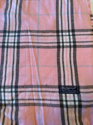 Rutig rosa halsduk från Burberrys - Snygg halsduk från Burberrys i klassiskt rutigt mönster med rosa, svart och vitt. Gjord av 100% lammull, mjuk och varm med fransar i kanterna. Perfekt accessoar för att lyfta din outfit med lite lyxig London-vibe.