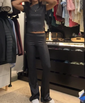 Svarta glittriga bootcut byxor - Säljer ett par svarta glittriga byxor med bootcut-snitt och hög midja. Materialet har en skimrande yta 