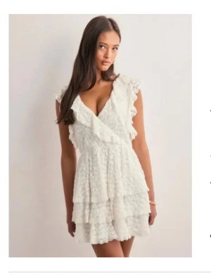 Vit spetsklänning med volanger - Supersöt vit kort klänning i spets med omlott och djup v-ringning i fram samt i bak. Passar perfekt till student eller skolavslutning, var mycket populär förra året när jag tog studenten . Kom aldrig till användning under min studentdag tyvärr. Bara att fråga om fler bilder.    Ny utan prislapp. I strl XS❣️ 