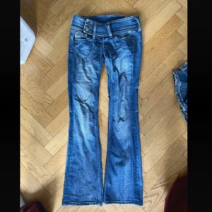 Lågmidjade bootcut disel jeans - Snygga disel jeans i klassisk blå tvätt med bootcut passform. Byxorna har knäppning med flera knappar fram, fem fickor och breda bälteshällor. Jeansen är tillverkade i slitstarkt denim och har en cool faded effekt på benen. Köpta i LA.