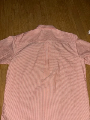 Rosa och vit randig skjorta - Snygg skjorta med smala rosa och vita ränder, klassisk krage och långa ärmar med manschett och knappar. Skjortan har en normal passform och är gjord i mjuk bomull som känns skön mot huden. Perfekt för dig som gillar stilrena detaljer och fräscha färger. Från Volt.