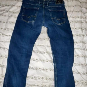 Blå Replay Anbass jeans herr - Säljer ett par klassiska blå jeans från Replay, modell Anbass. Jeansen har raka ben, snygga bakfickor med dekorativa sömmar och detaljer i kontrastfärg. Tillverkade i slitstarkt denim med normal passform och medelhög midja.