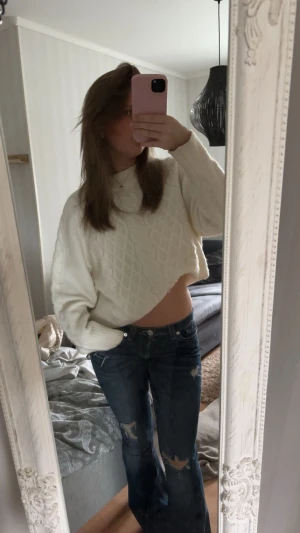 Vit croppad stickad tröja - Säljer en vit croppad stickad tröja med rutmönster. Tröjan har lång ärm, rund hals och en loose fit som ger en chill vibe. Perfekt att matcha med jeans eller mönstrade byxor för en trendig look.