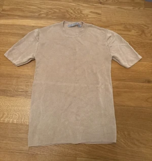 Beige stickad tröja Tiger of Sweden - Snygg beige stickad tröja från Tiger of Sweden, modell Ella. Tröjan har rund hals, korta ärmar och är gjord i mjukt stickat material. Perfekt för dig som gillar stilrena och enkla plagg med en clean vibe.