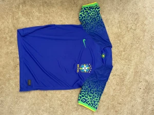 Blå Brasilien fotbollströja Nike - Snygg blå Brasilien fotbollströja från Nike med korta ärmar. Ärmarna har ett unikt leopardmönster i grönt och blått med gula detaljer vid ärmslut. Tröjan har Brasilien-emblem och Nike-logga på bröstet. Tillverkad i lätt och ventilerande material.