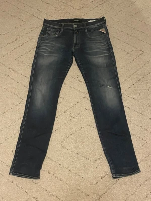 Replay Anbass jeans blå slim fit - Snygga Replay Anbass jeans i mörkblå tvätt med slitningar och klassiska fem fickor. Slim fit-modell med låg midja och raka ben. Jeansen har Replay-logga på fickan och bakre läderpatch. Perfekt för dig som gillar en modern och stilren look. Pris går att diskutera!!