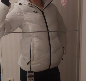 Helr ny Dam Vit pufferjacka från Tuxer - strl S - Säljer en snygg vit pufferjacka från Tuxer med svart dragkedja och fickor med dragkedja. Jackan har hög krage och en stilren, quiltad design som håller dig varm under kalla dagar. Perfekt för dig som vill ha en clean och modern look. Ny med prislapp